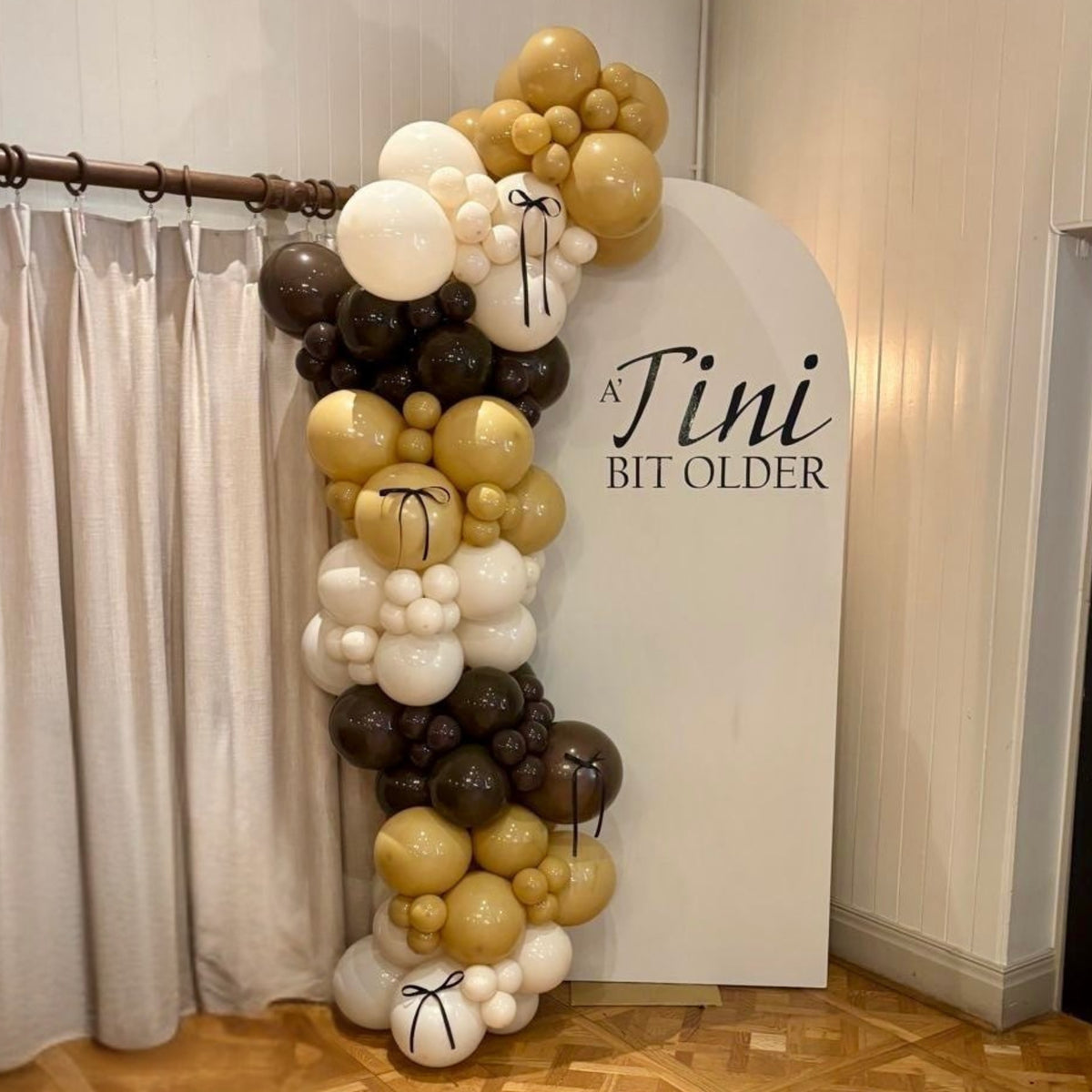 Sailboard with Personalised Vinyl Print and Cream Pastel Dusk, Latte & Chocolate Balloon Garland with Black Bow Detail